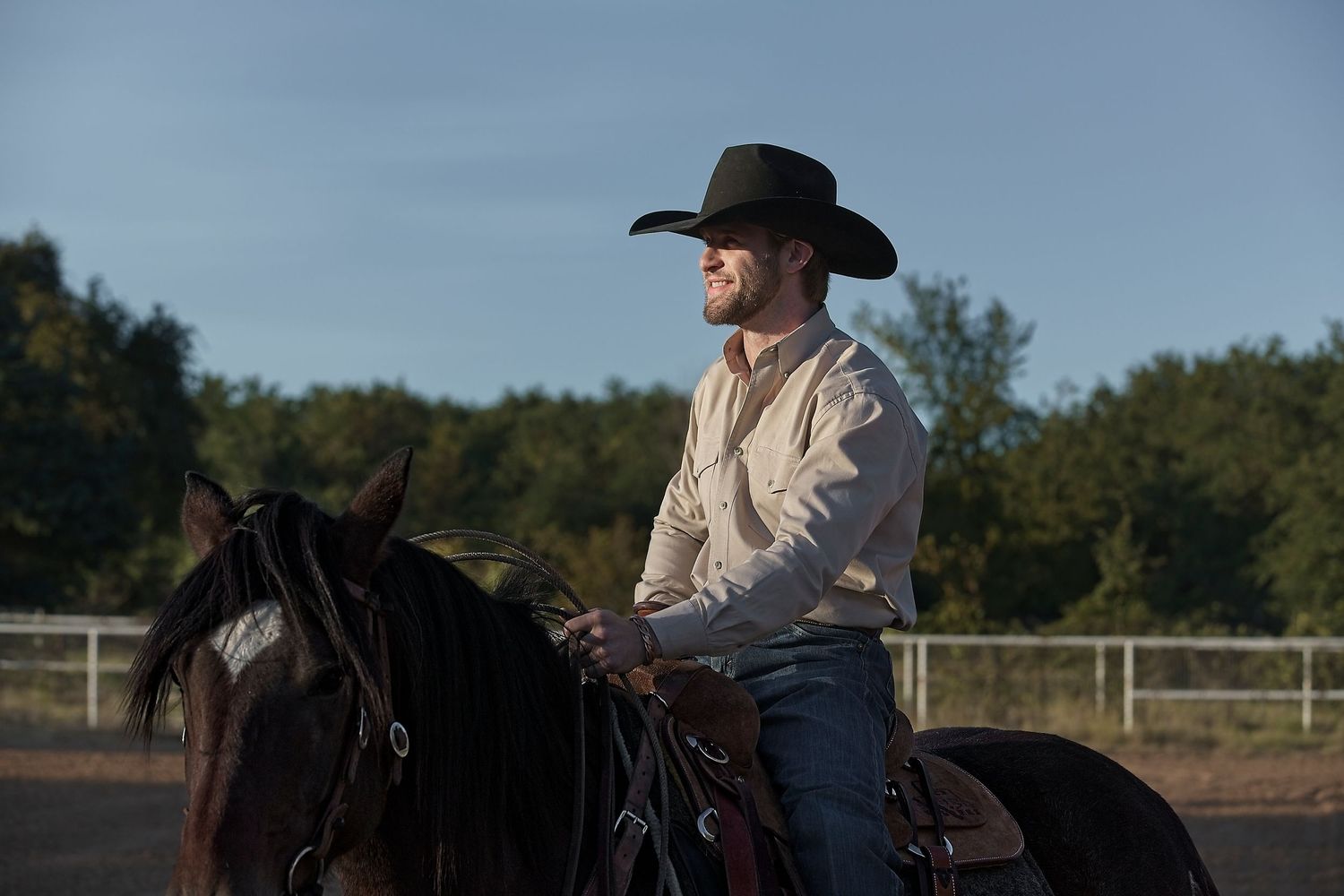 A horseback rider in traditional Western clothing guides their horse in an outdoor arena.