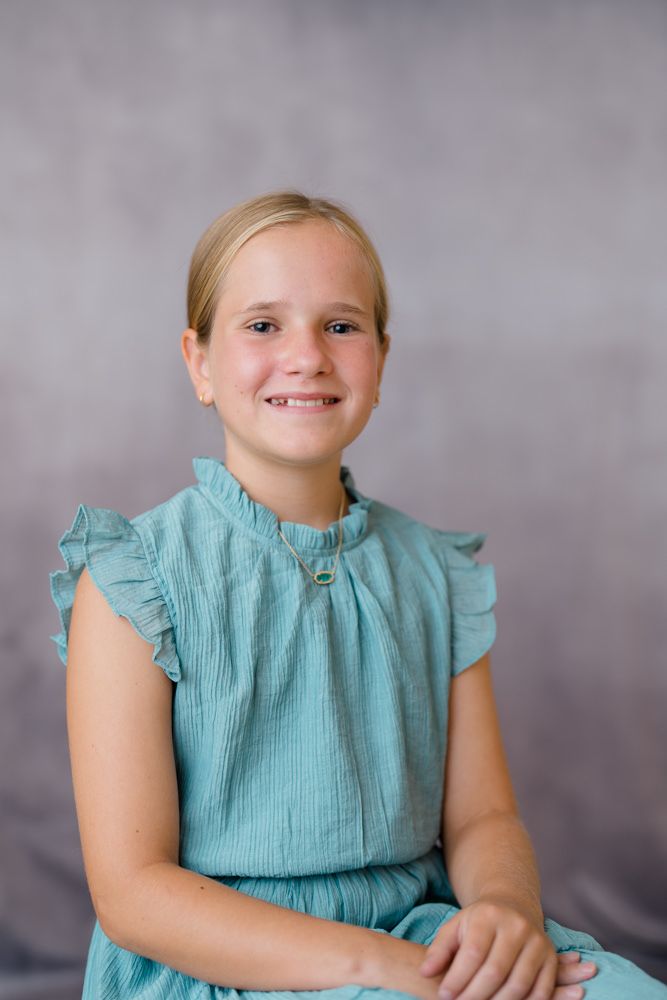 Child wearing a teal ruffled sleeve dress poses against a gray backdrop in a series of portrait shots.