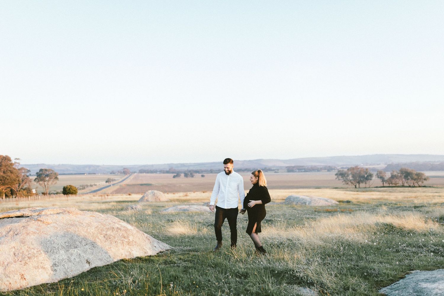 Two people stand together on a rugged overlook with expansive views of the countryside.