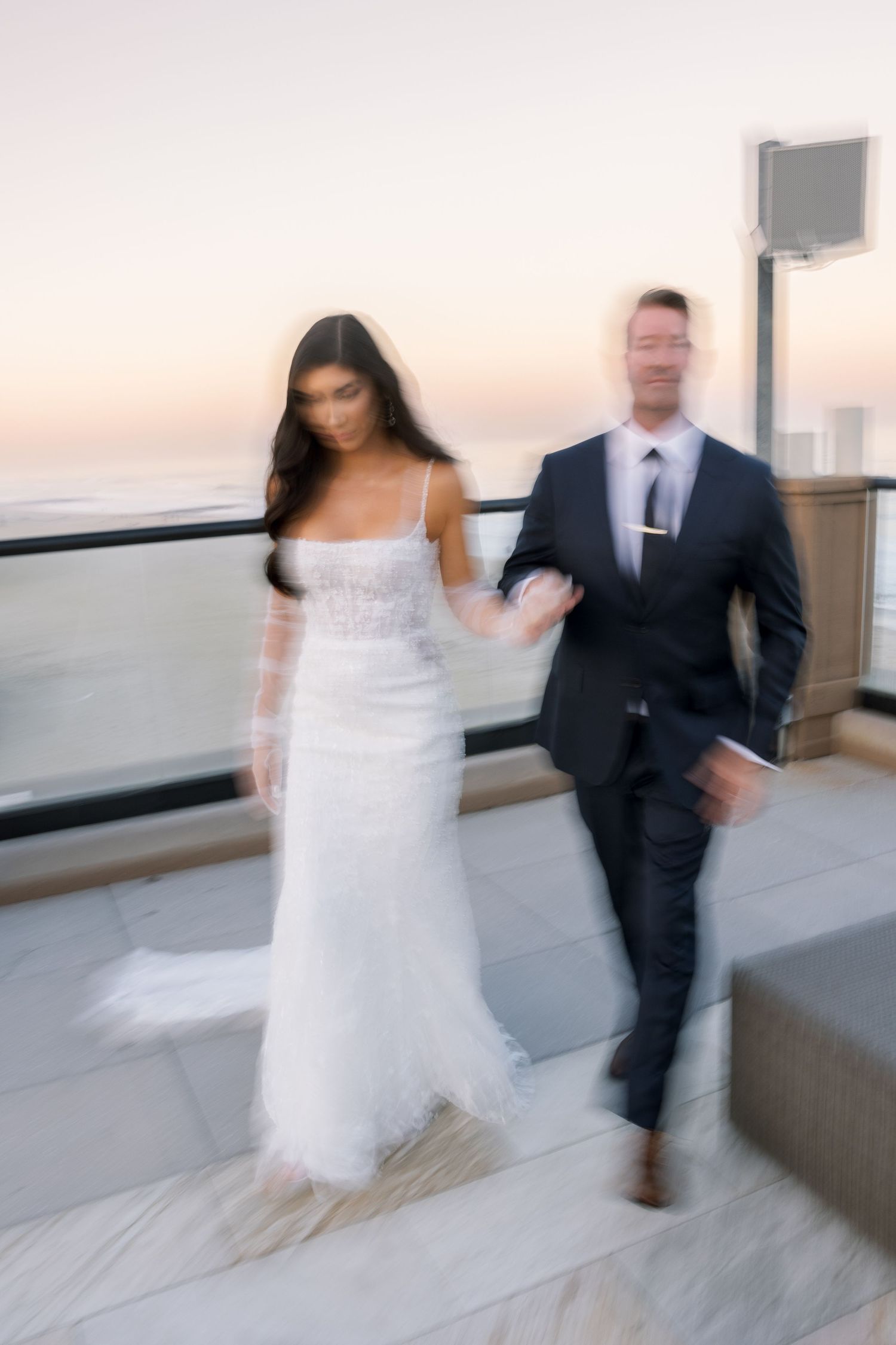 Motion-blurred photo of a couple walking together on a seaside terrace at sunset.