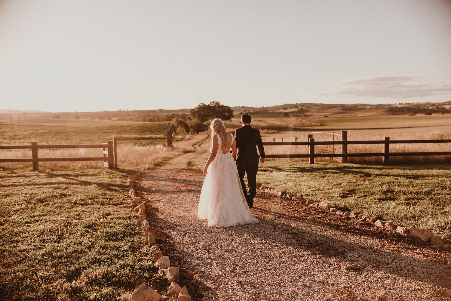 Wedding couple walking toward sunset holding hands in Bathurst at Boxgrove walking across field down dirt road