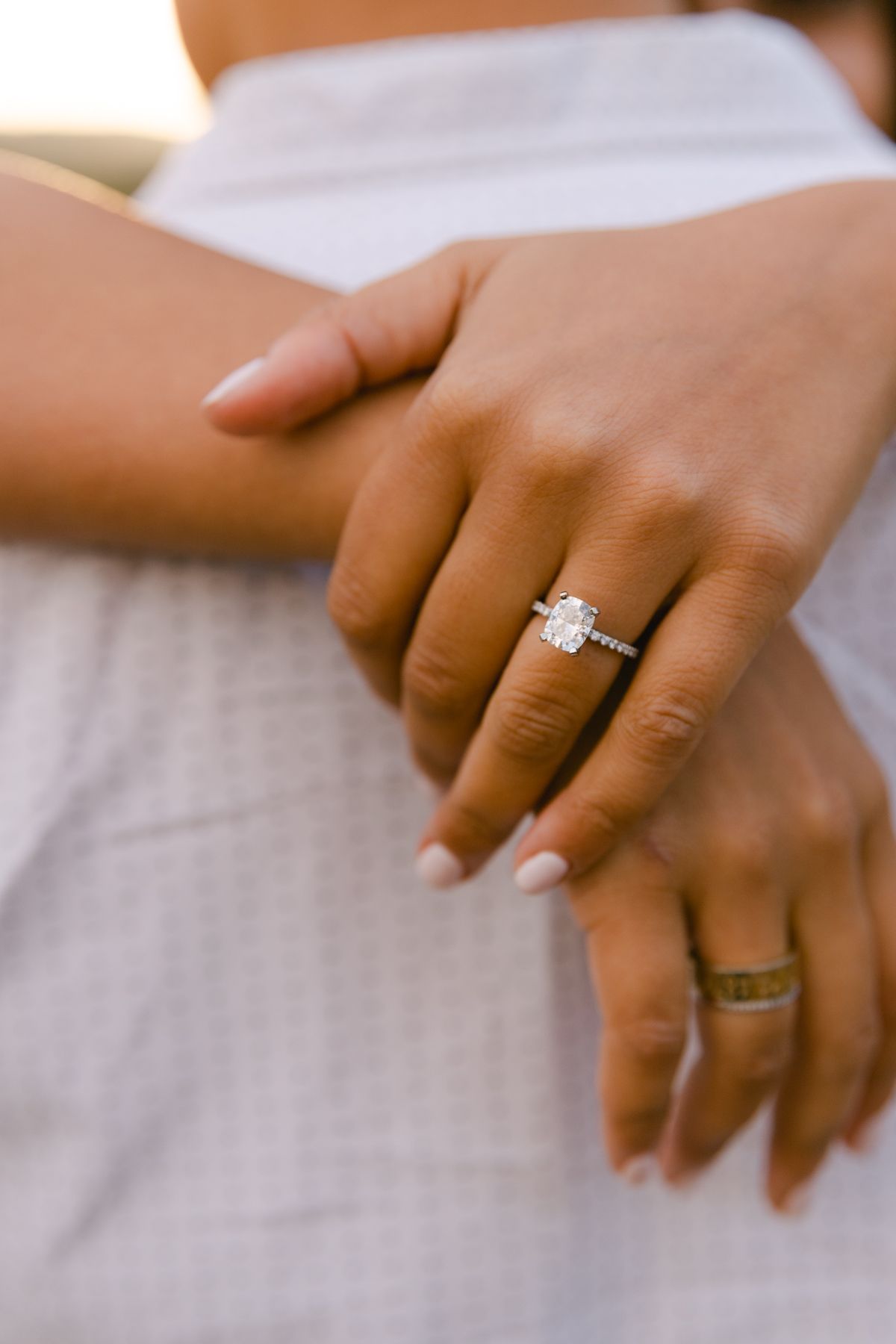 A woman's hands are resting on the back of a man's neck. There's an engagement ring on her finger and her nails are painted light pink.