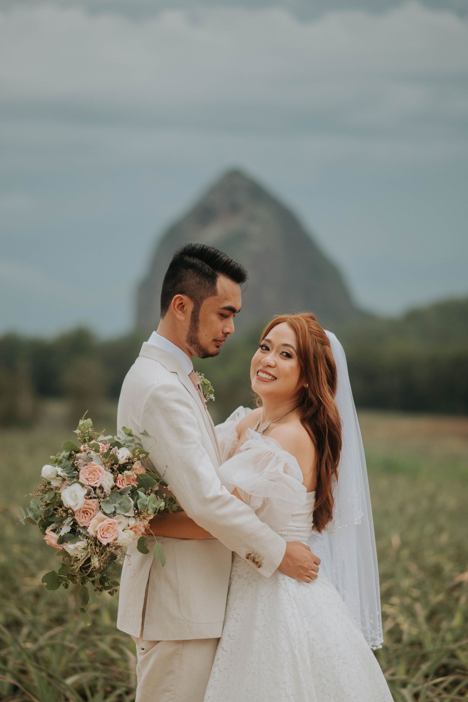 Newlyweds share an intimate moment in a field with a majestic mountain backdrop.