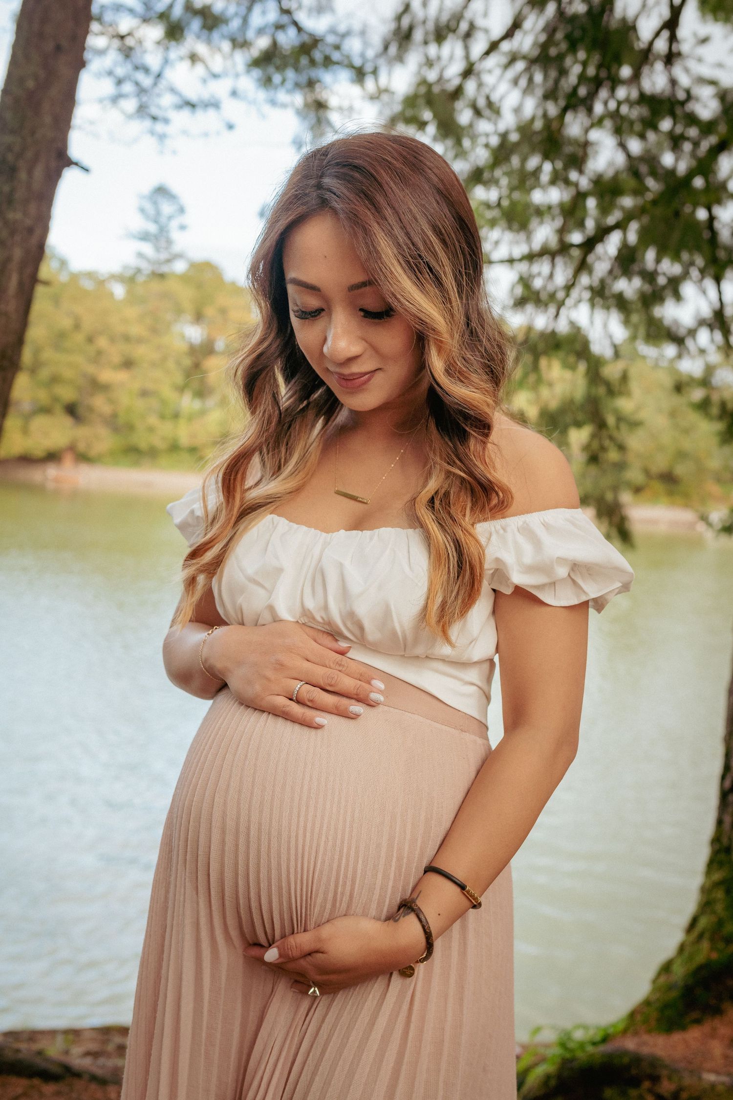 Pregnant woman in white off-shoulder dress by lake, Portland Oregon maternity session in soft fall light.