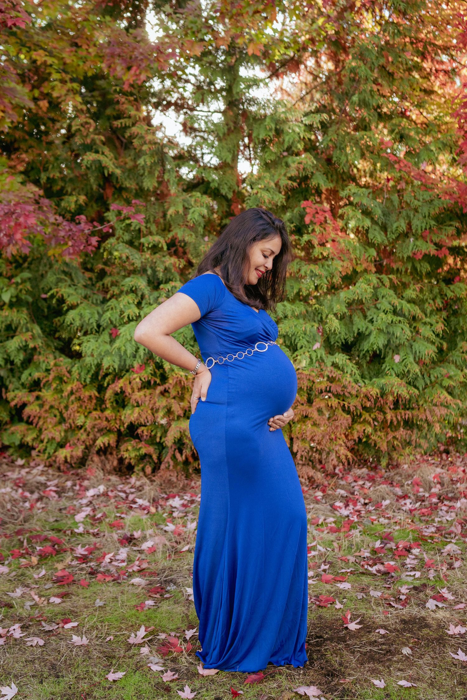 Pregnant woman in bold blue dress with colorful autumn leaves, Portland Oregon maternity portrait session.