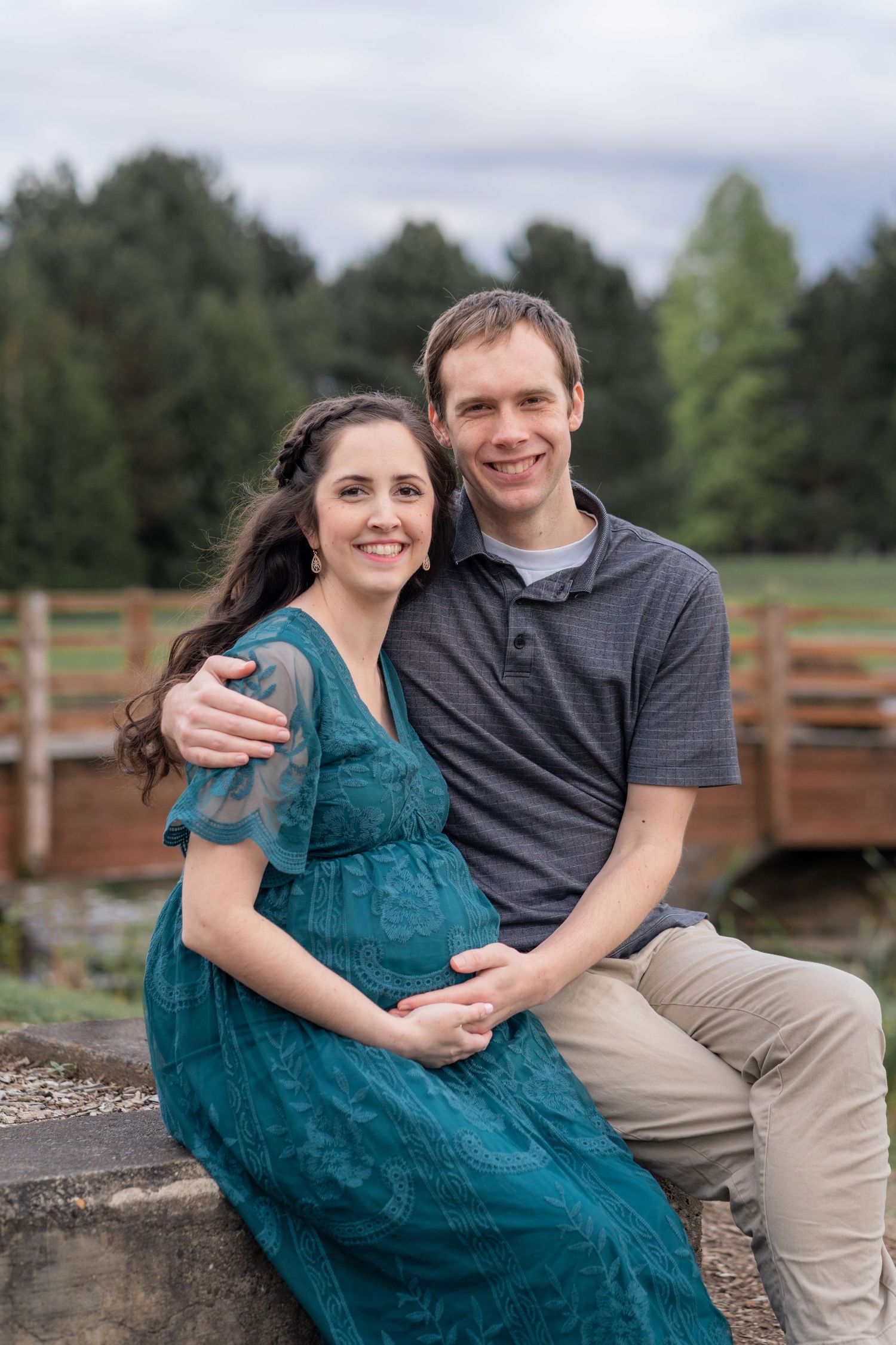 Couple holding belly, wood bridge in the background, in PNW forest, maternity session in Washington State park.