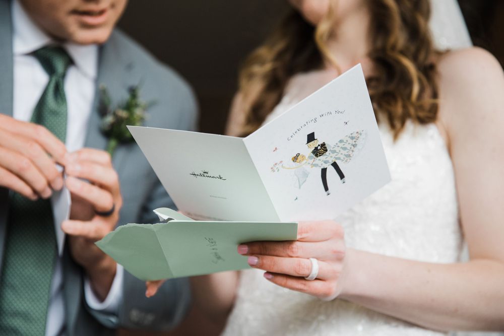 A bride and groom reading a wedding card together with a green boutonniere detail.