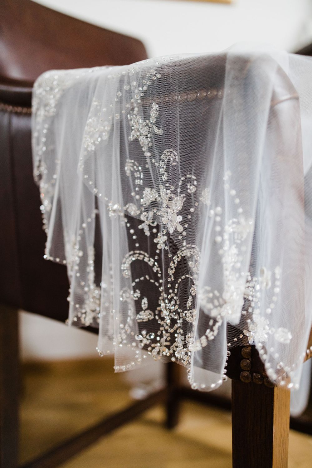 Delicate beaded lace veil with floral patterns draped over a brown chair.