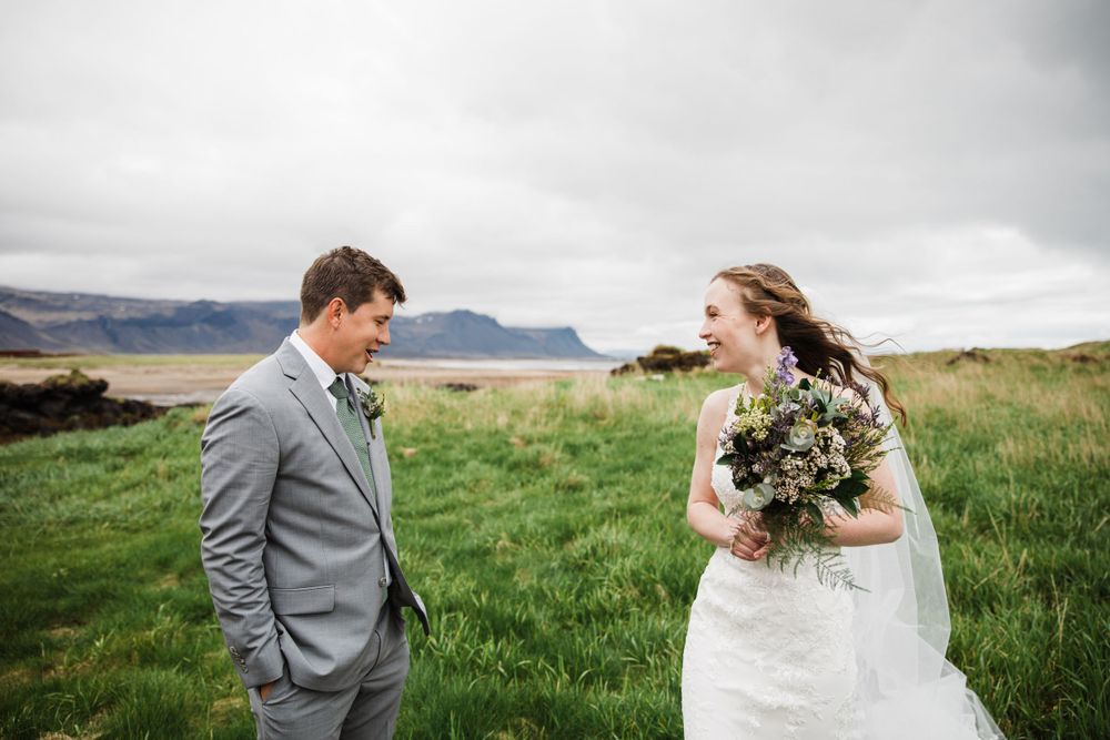 Wedding couple shares moment in windy field with mountains in background.