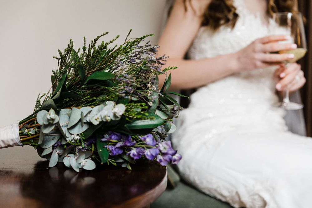 An artful bouquet of eucalyptus, purple flowers and greenery sits beside white fabric.