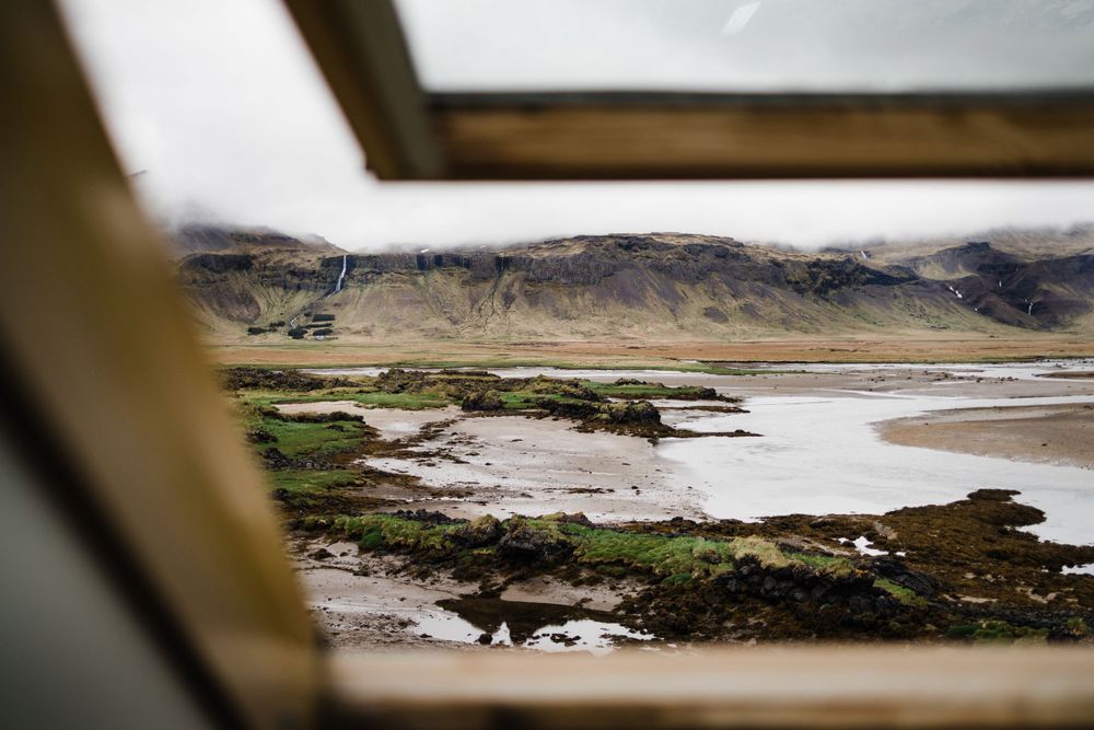Scenic view of an Icelandic coastline with mountains and sandy beach seen through a window frame.