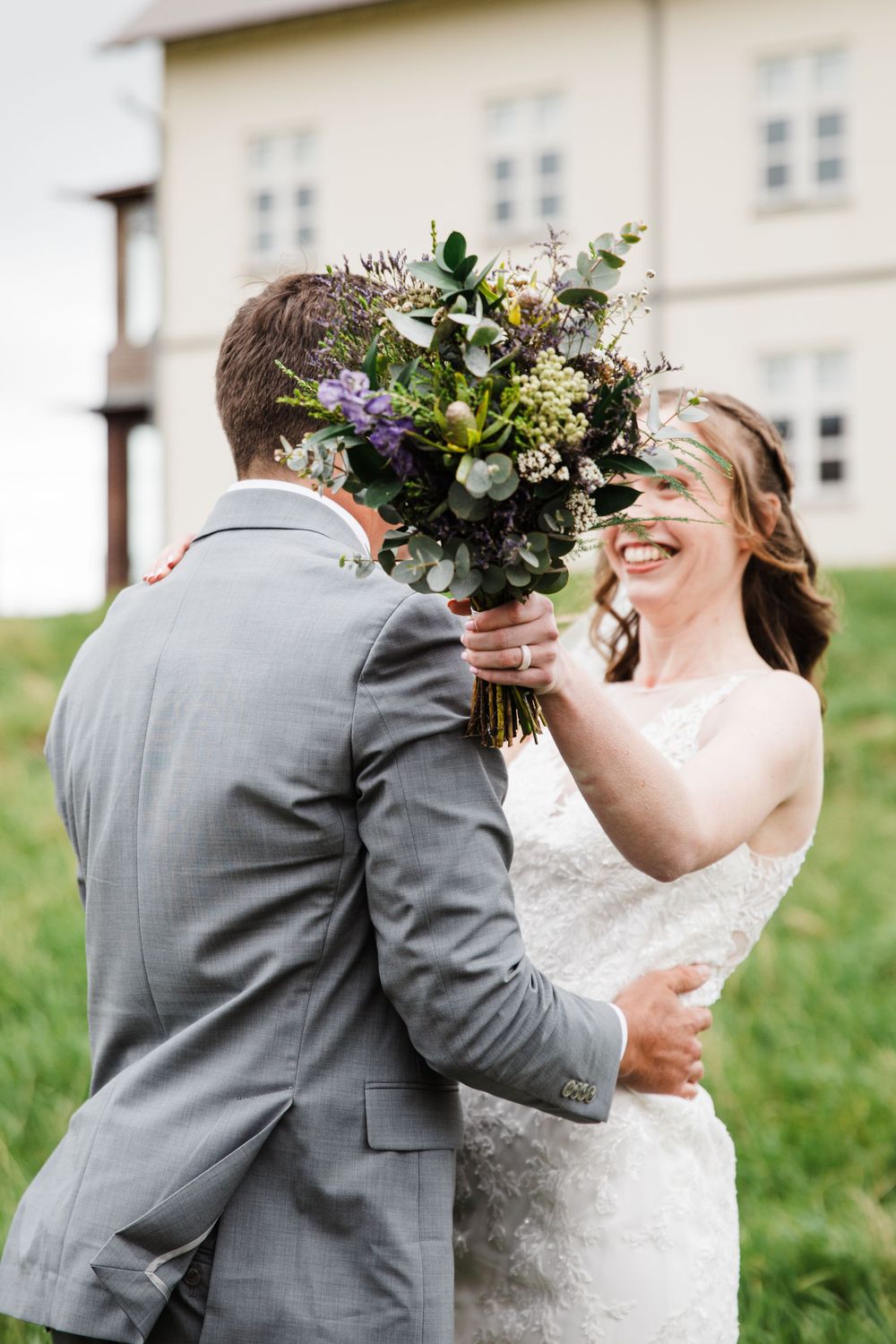 Wedding moment captured with wildflower bouquet in front of cream colored building.