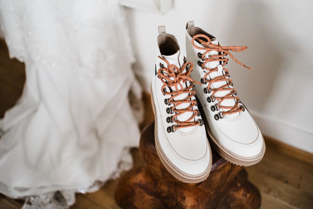 White leather hiking boots with orange laces next to flowing wedding dress fabric.