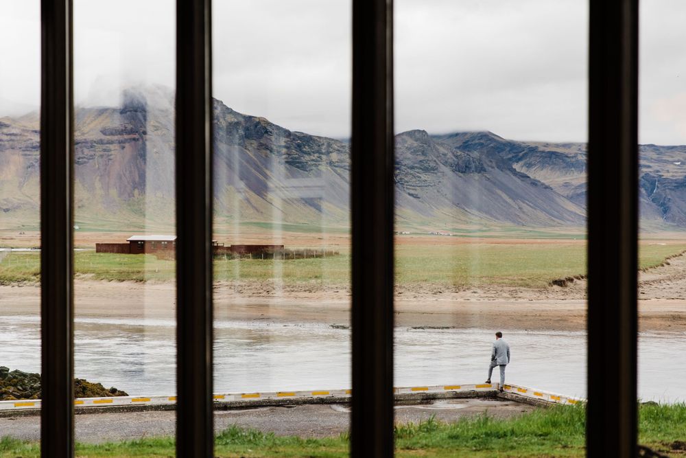 Scenic mountain landscape viewed through vertical window bars with a distant figure.