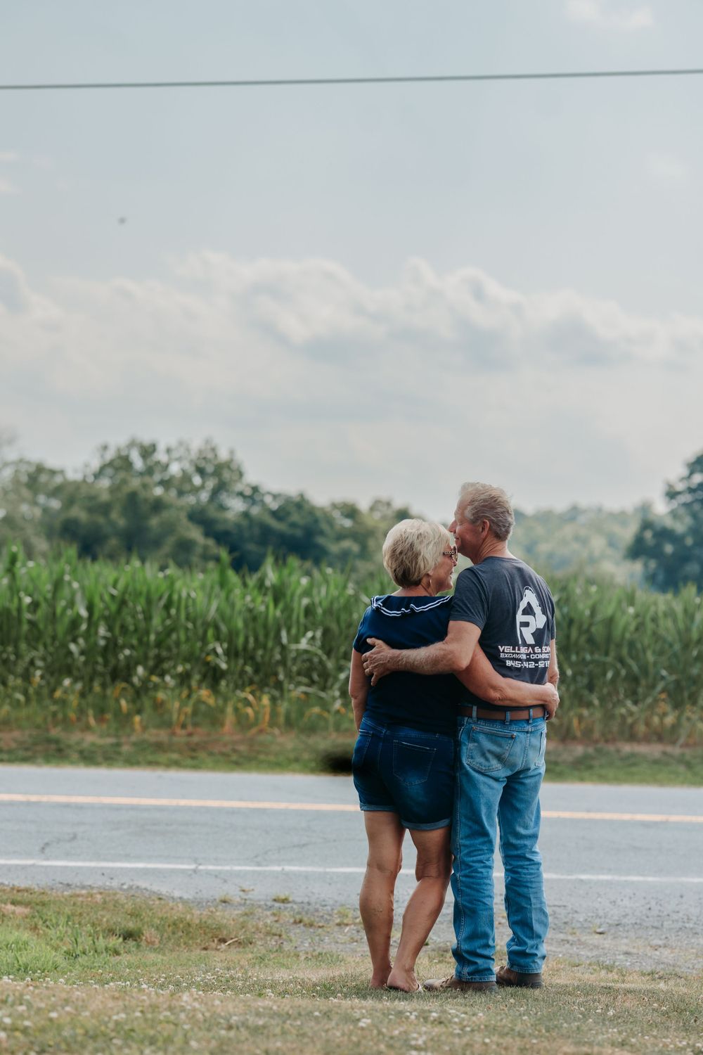 Couple standing together overlooking rural cornfield on sunny day.
