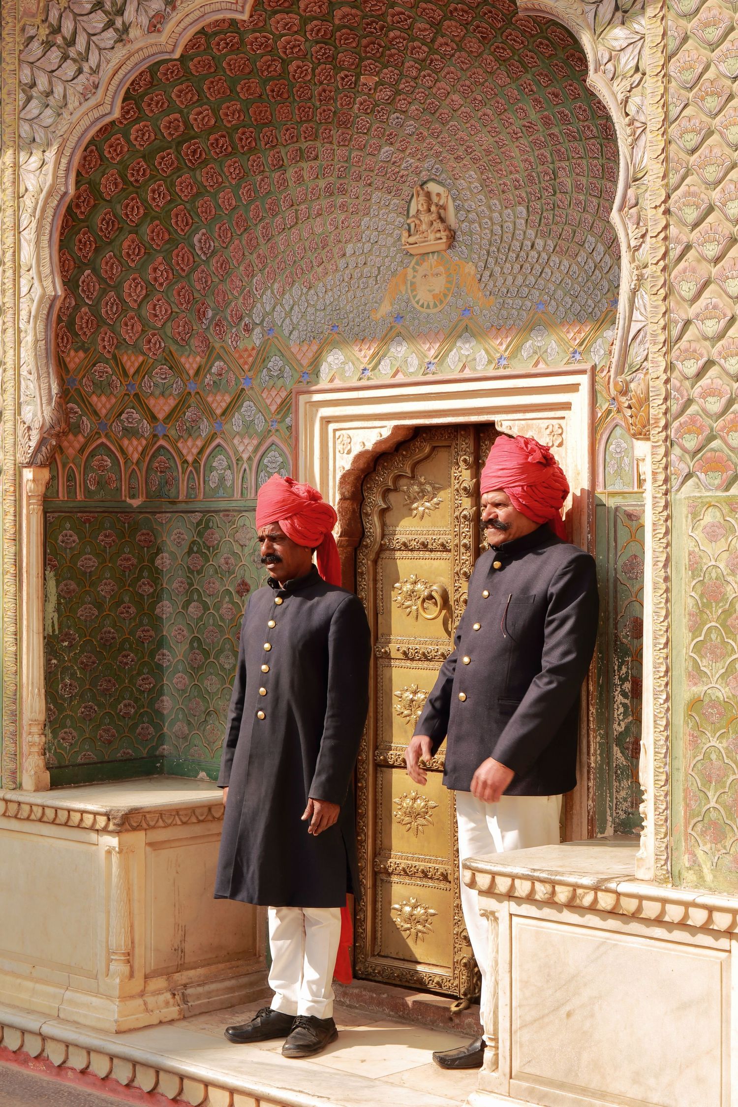 Ornately decorated entrance with guards in traditional uniforms and red turbans standing at a palace door.