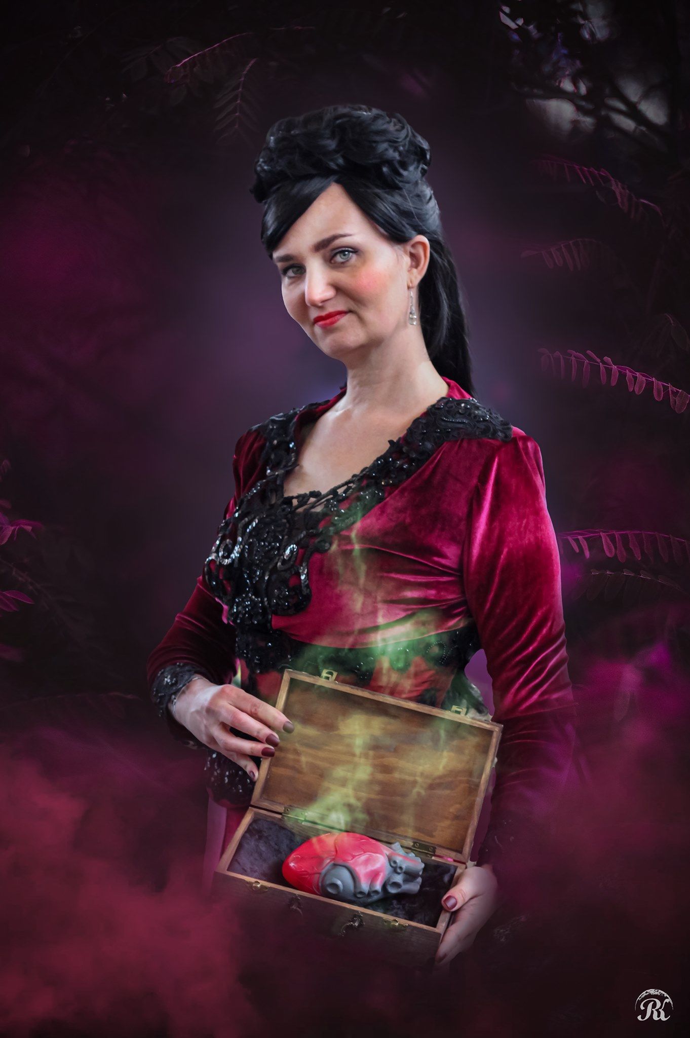 Dark-haired woman in red velvet dress holds antique wooden box in mystical purple themed portrait setting.