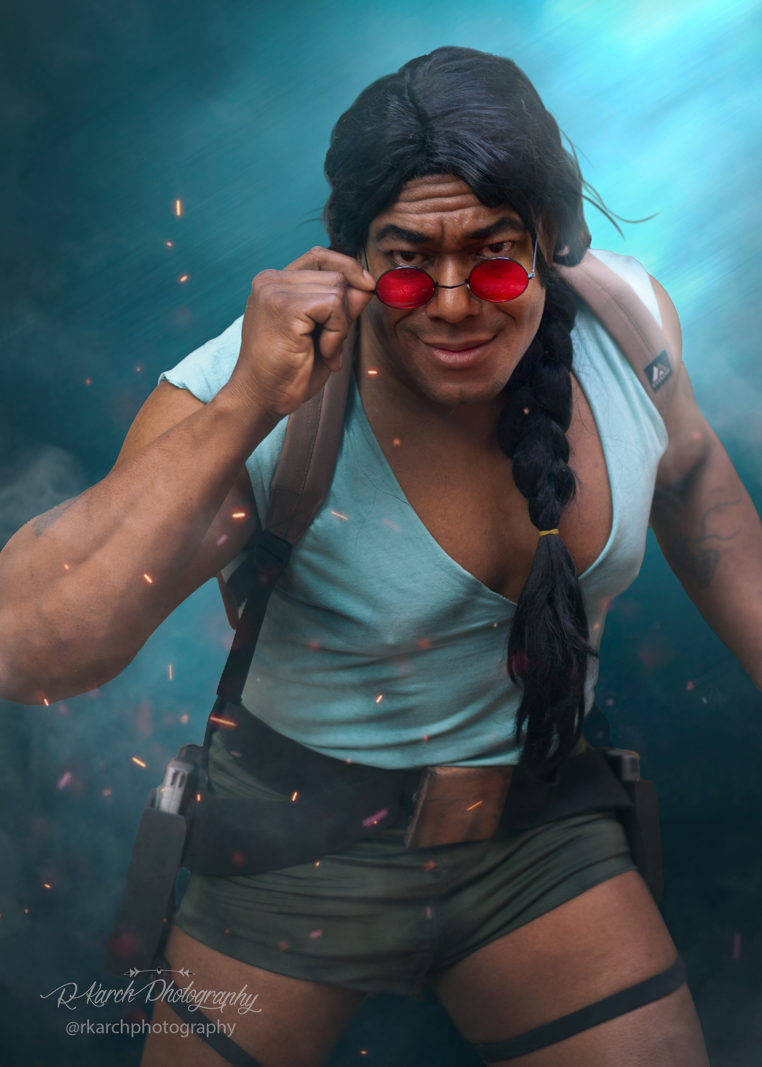 Cosplay model wearing a white tank top and red sunglasses strikes a dynamic pose against a blue backdrop.