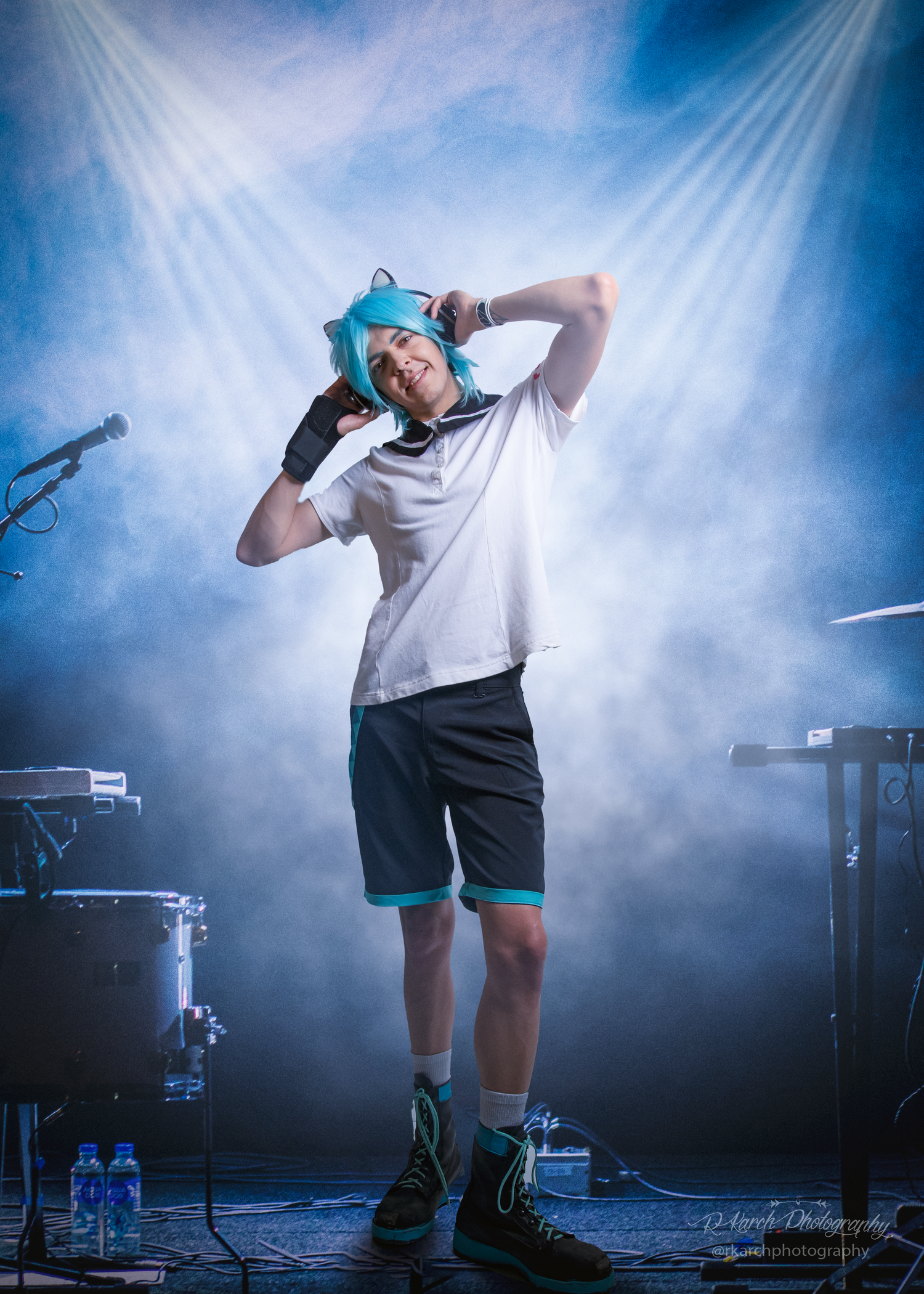 Figure in casual attire poses dramatically on stage with blue lighting and smoke effects.