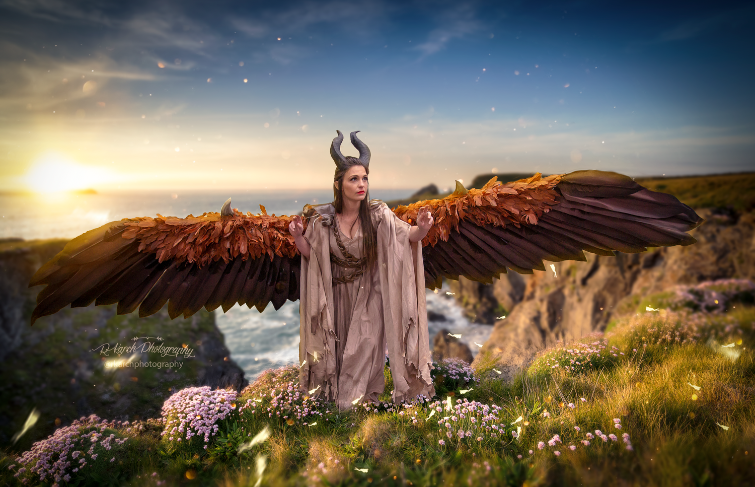 Fantasy character with large brown wings poses in flowing robe against sunset mountain landscape.