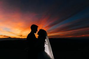 Silhouettes of a couple sharing an intimate moment against a dramatic sunset sky with vibrant orange clouds.