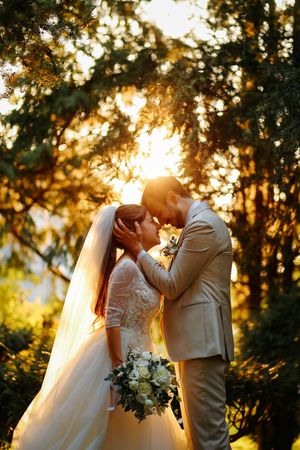 Newlyweds share a romantic kiss in golden hour sunlight filtering through forest trees in an October sunset wedding