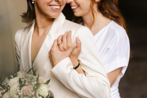 Close-up of couple in white outfits holding hands and showing off engagement ring.