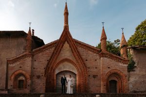 Couple stands in silhouette under Gothic brick archways of historic church architecture.