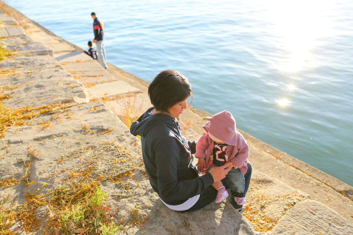 People sitting along a waterfront watching the sunset over sparkling water.