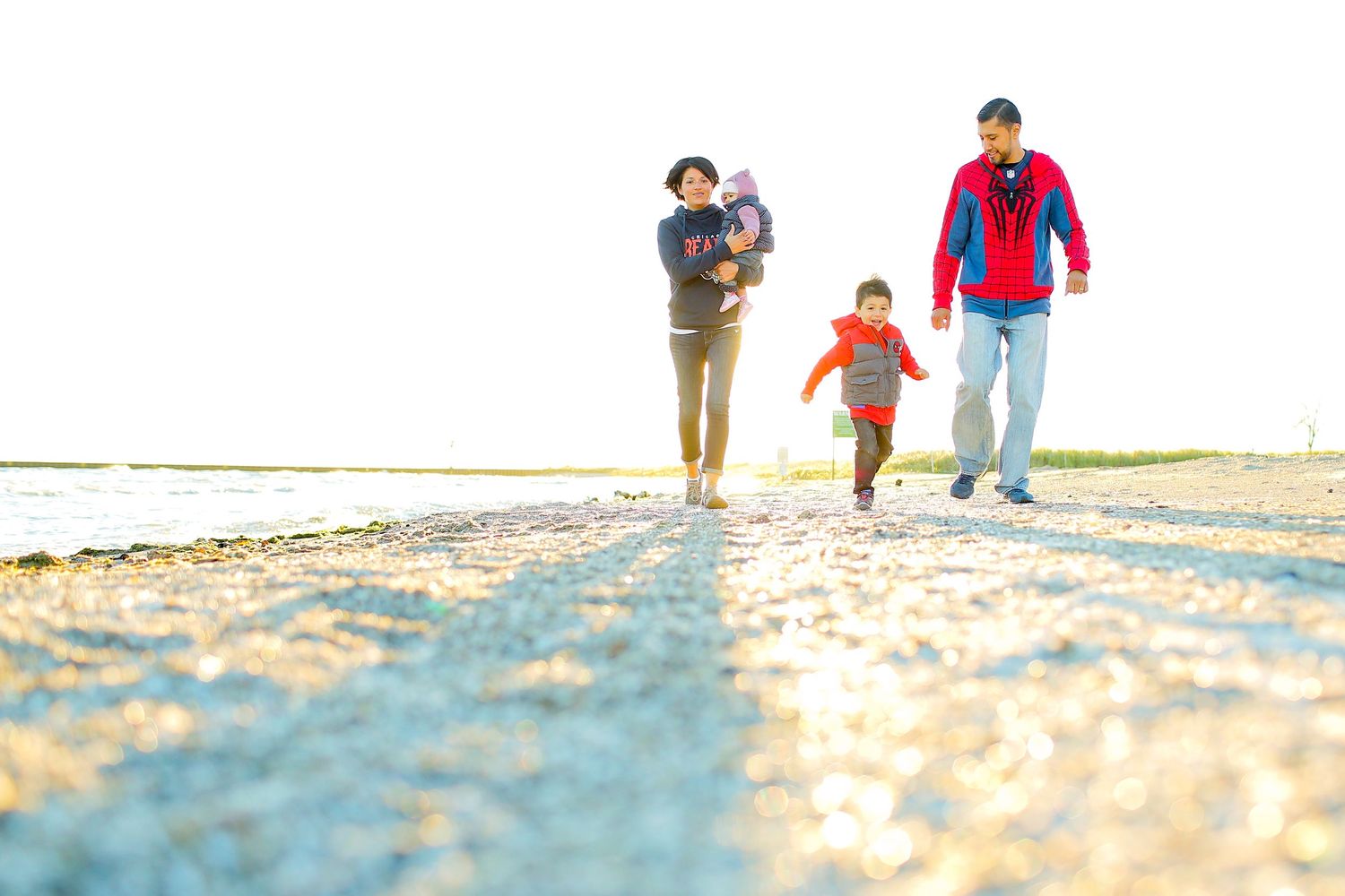 Family walking together along a sunny beach with golden sand and clear skies.