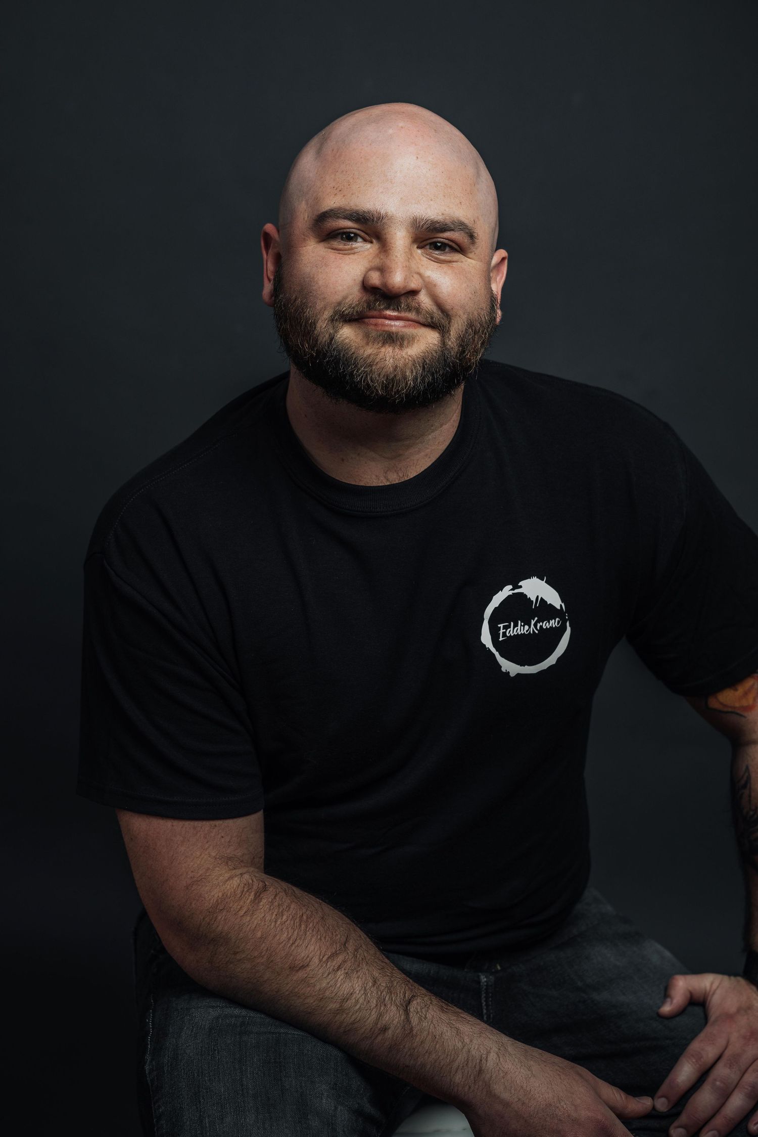 Professional headshot of person in black t-shirt with company logo against dark background.