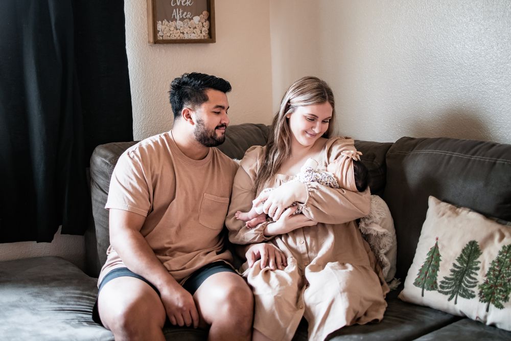 Intimate indoor family moment on grey couch with newborn in casual home setting.