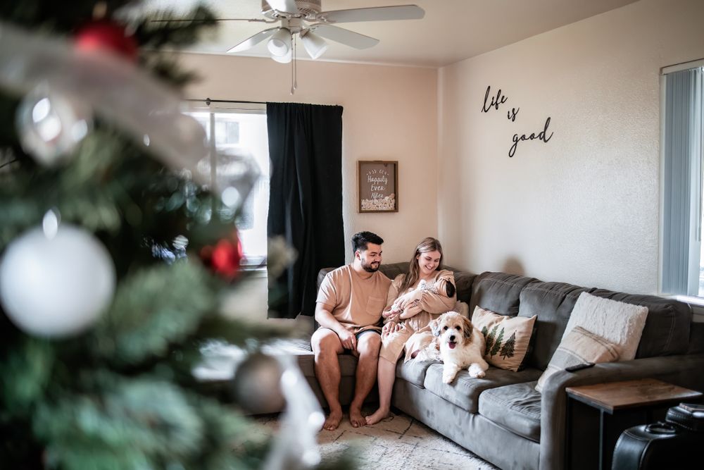 A couple sits on a gray couch near a decorated Christmas tree in a cozy living room.