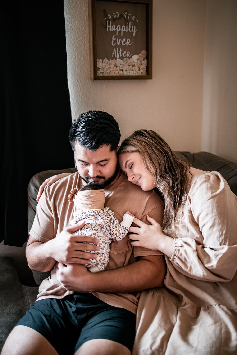 A couple shares an intimate family moment on their couch beneath a decorative wall sign.