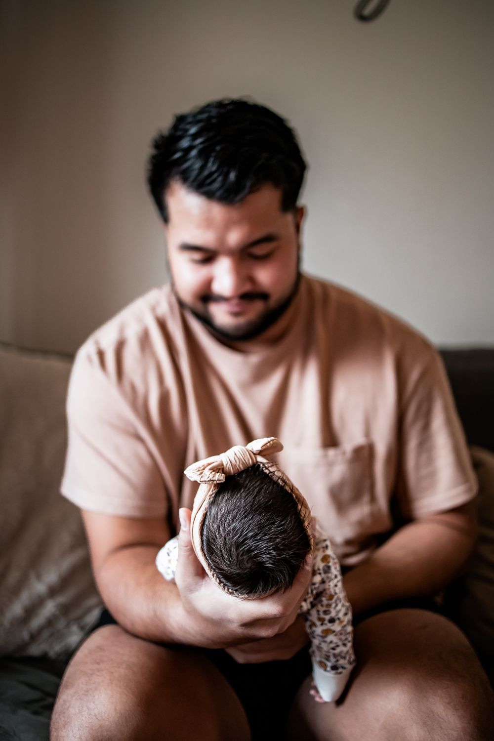 Parent gazes lovingly at newborn baby while sitting on gray living room couch.