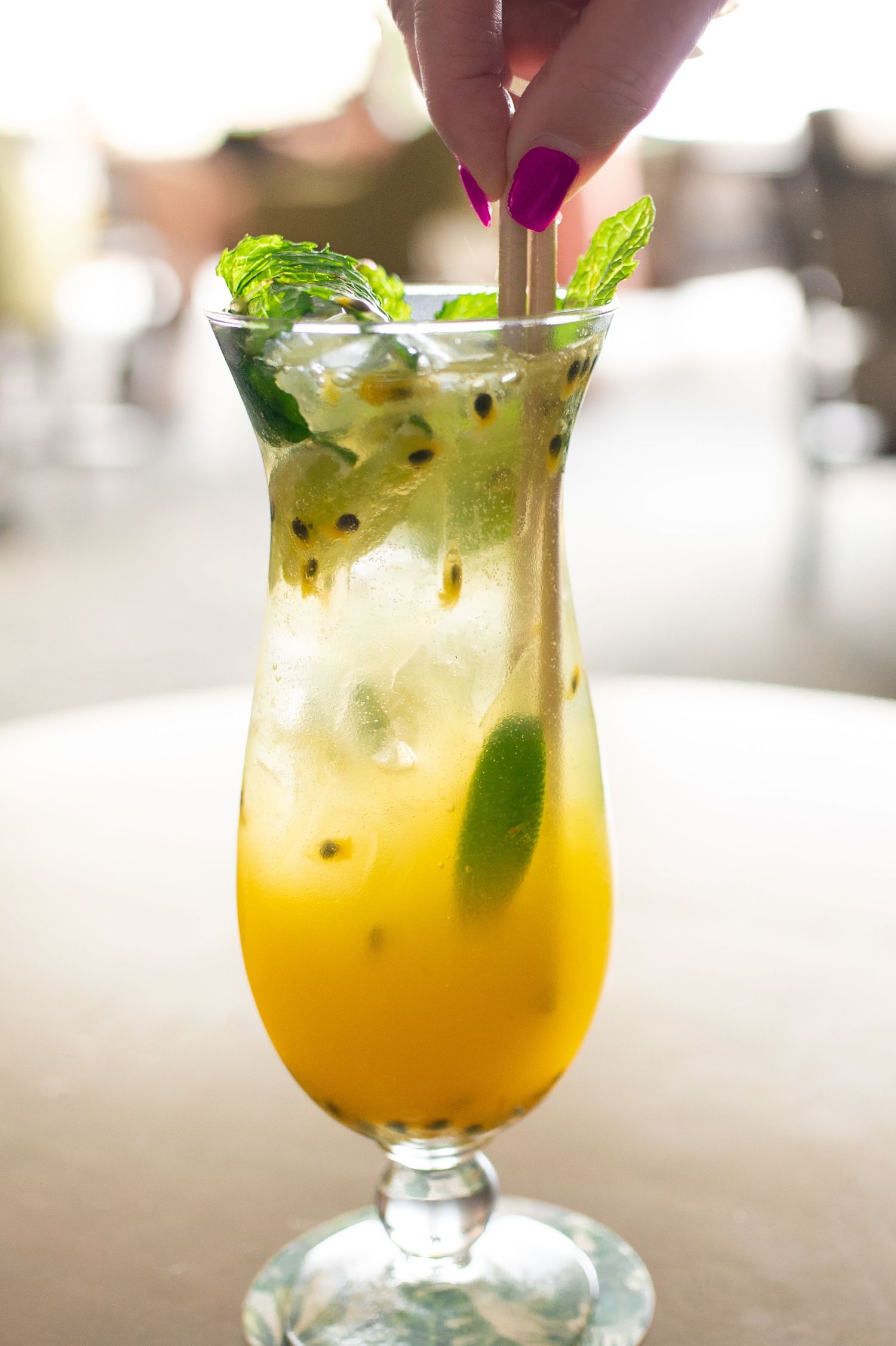 Tropical passion fruit cocktail garnished with fresh mint leaves and lime in a hurricane glass.
