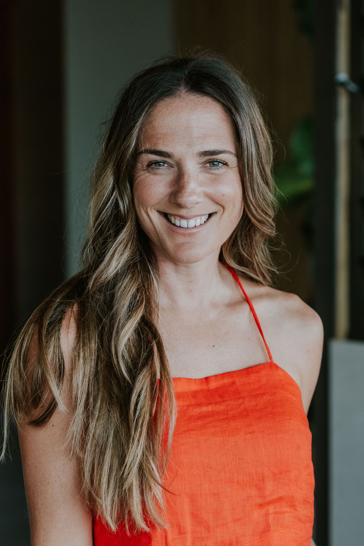 Portrait of someone wearing a vibrant orange top with long wavy hair against a dark background.