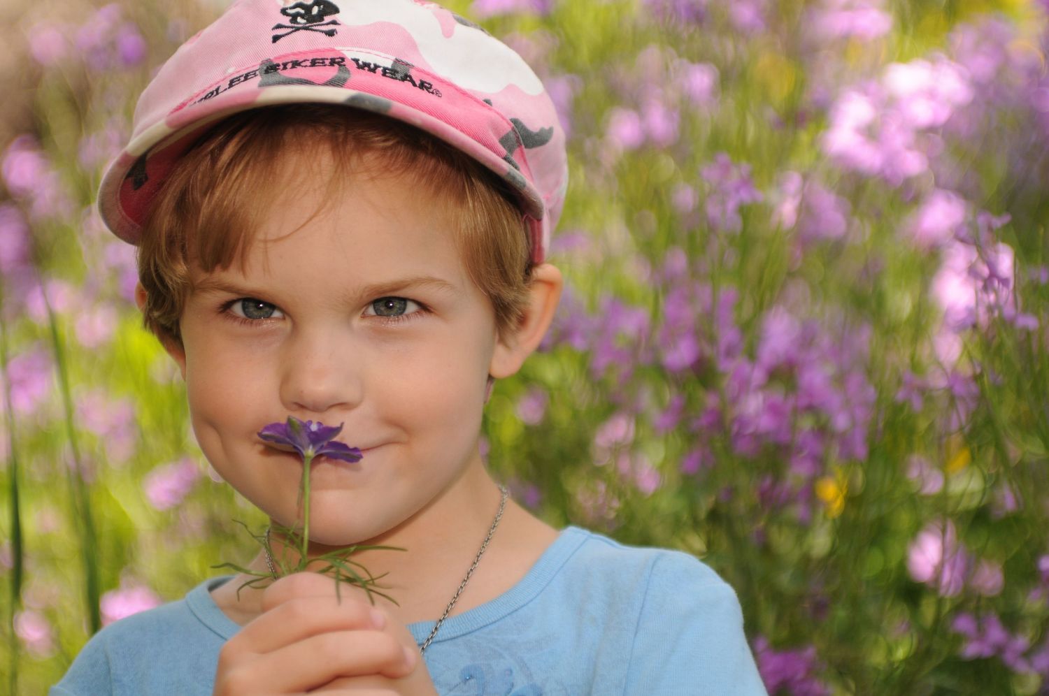 Young girl smelling purple wildflower posing in a garden