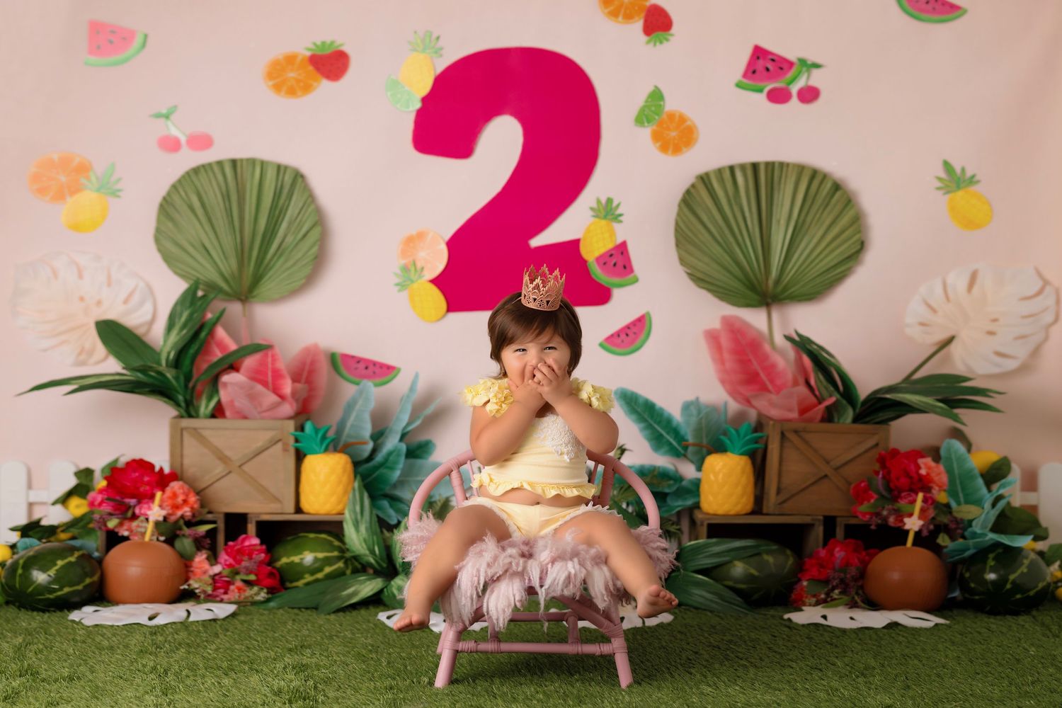 Whimsical birthday setup with pink backdrop, number 2, palm fans, and floral decorations for a special celebration.