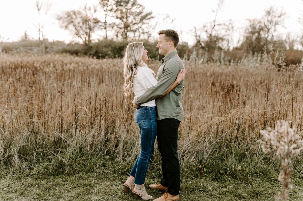 Romantic couple embracing in rustic field during golden hour.