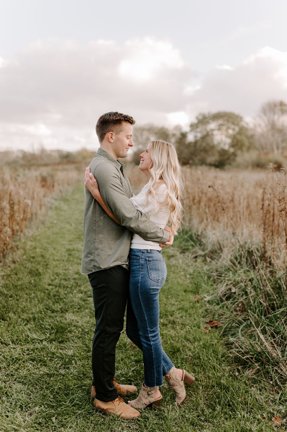 Intimate moment between couple standing in grassy meadow at sunset.