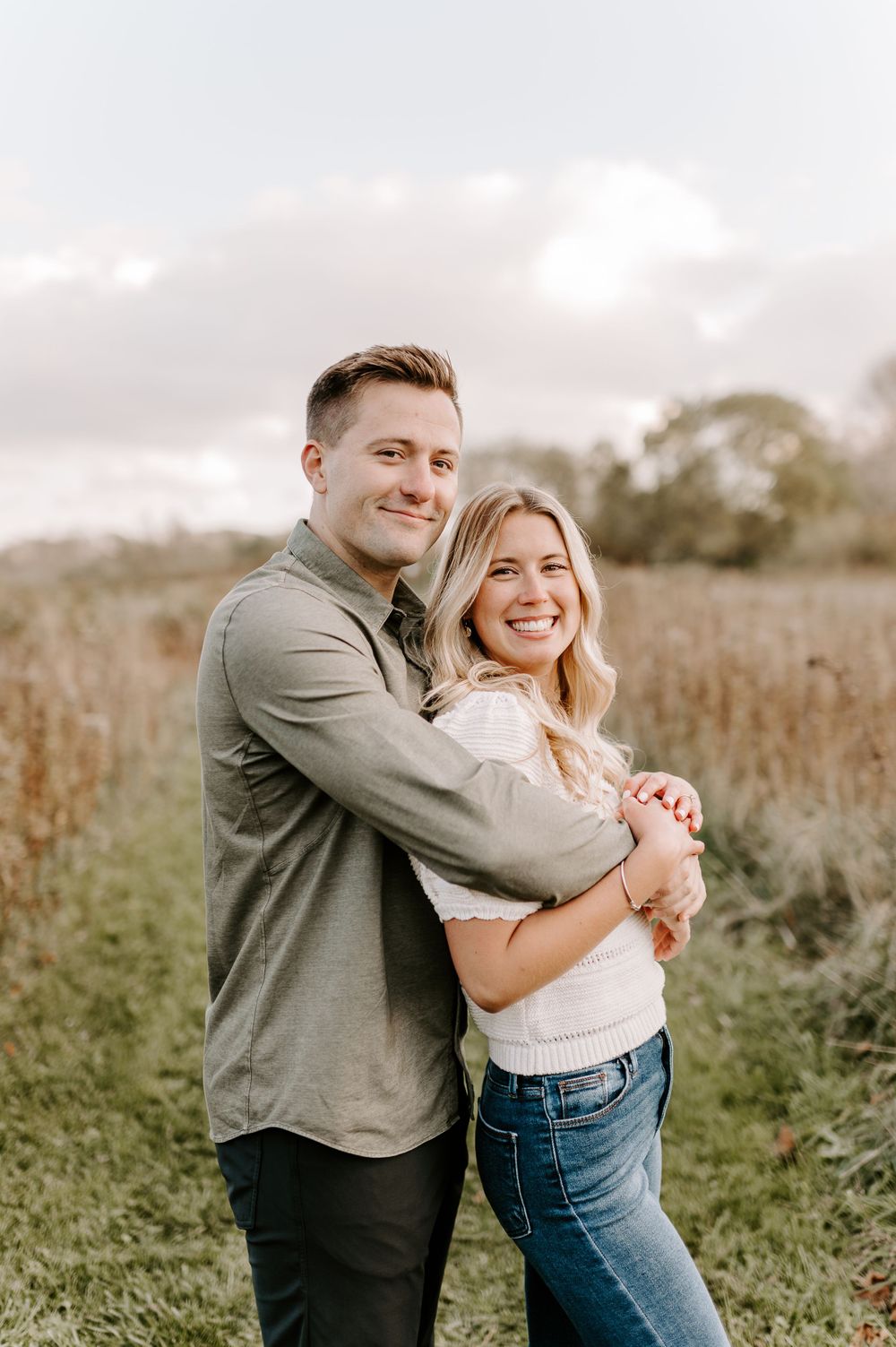 Couple sharing warm embrace while laughing in sunlit field.
