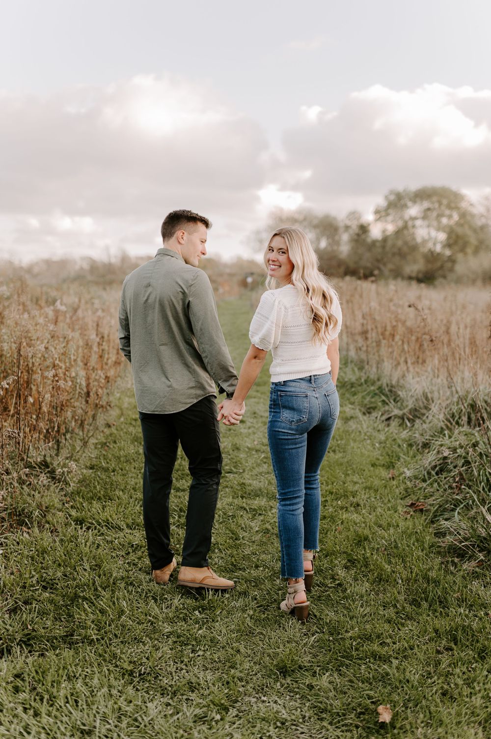 Couple walking hand in hand through natural pathway in field.