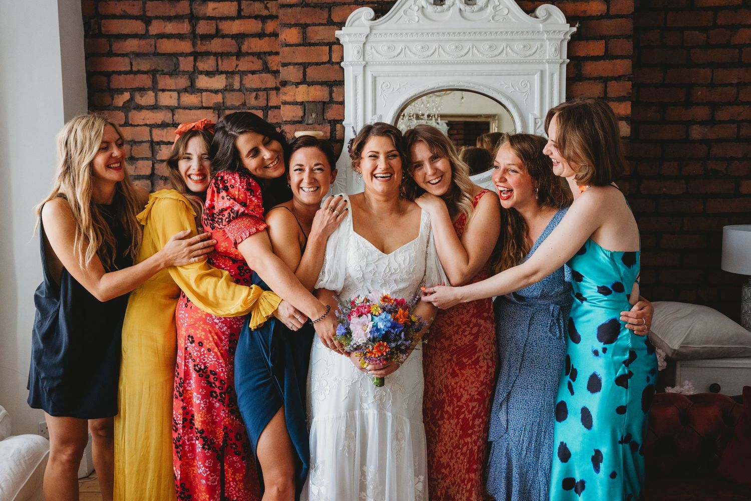 Group of bridesmaids in colorful dresses gather around bride for wedding photo.