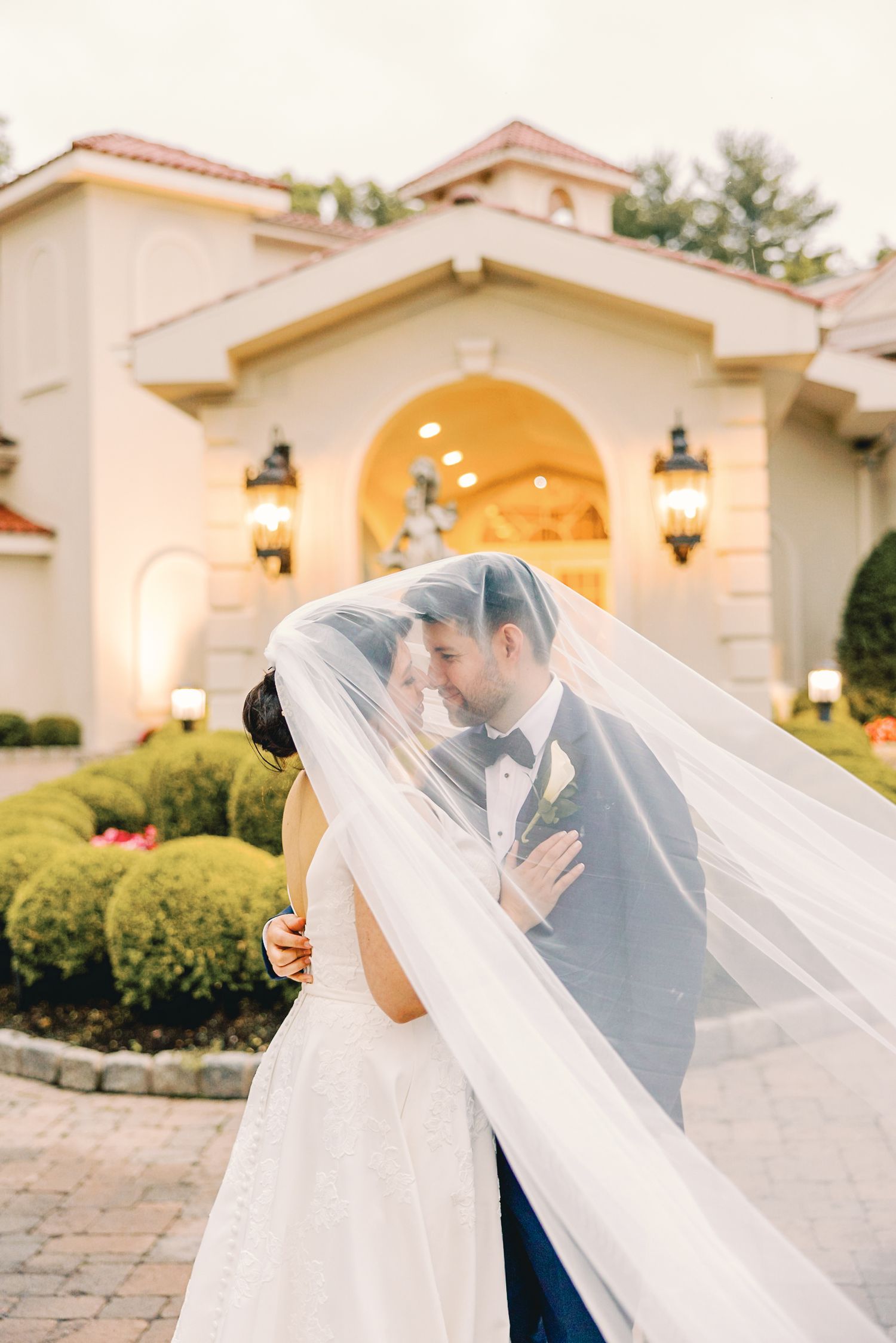 Bride and groom sharing an intimate moment under a flowing veil outside an elegant wedding venue.