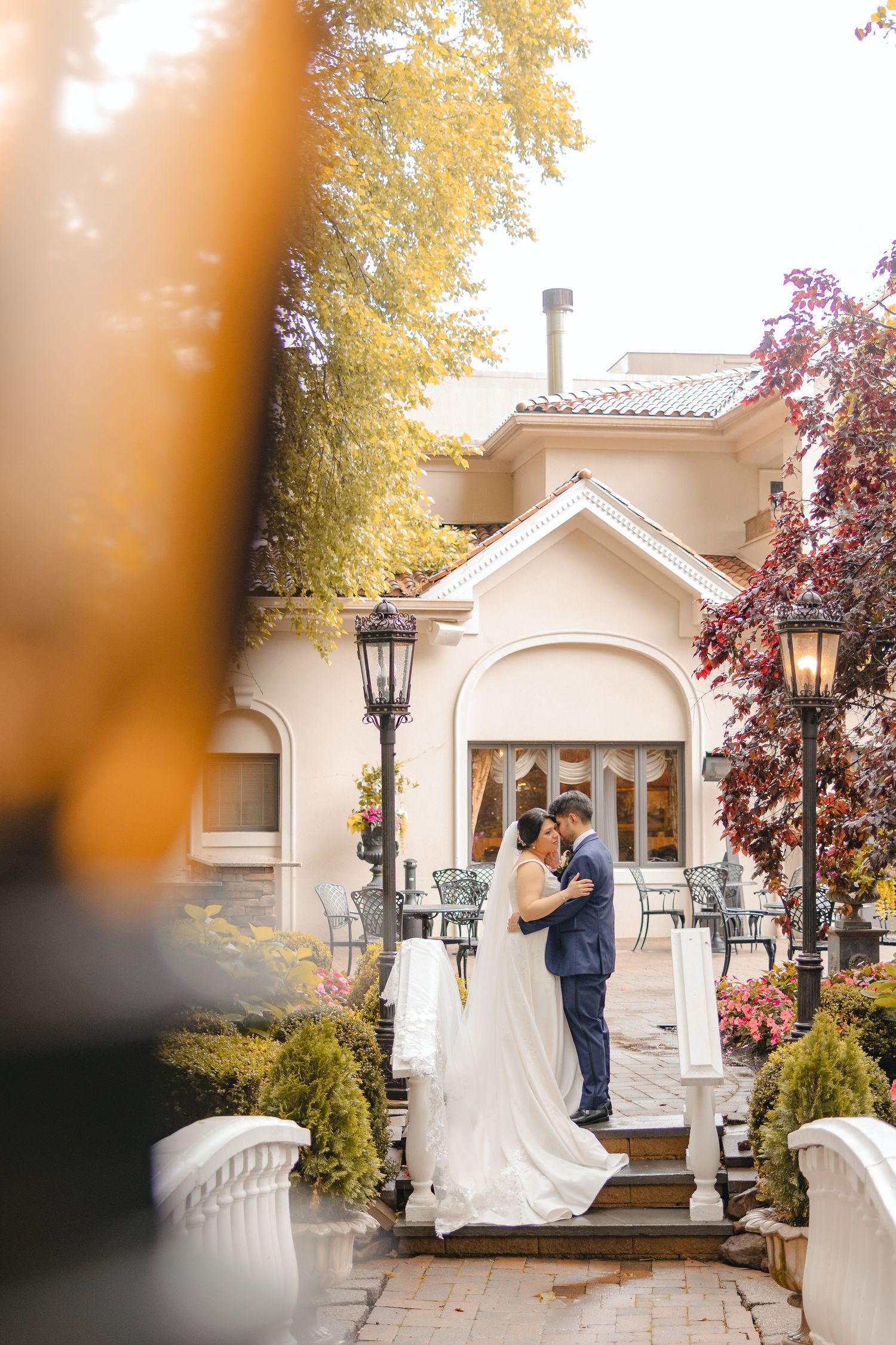 Bride and groom sharing a romantic embrace outside a elegant villa venue surrounded by autumn foliage.