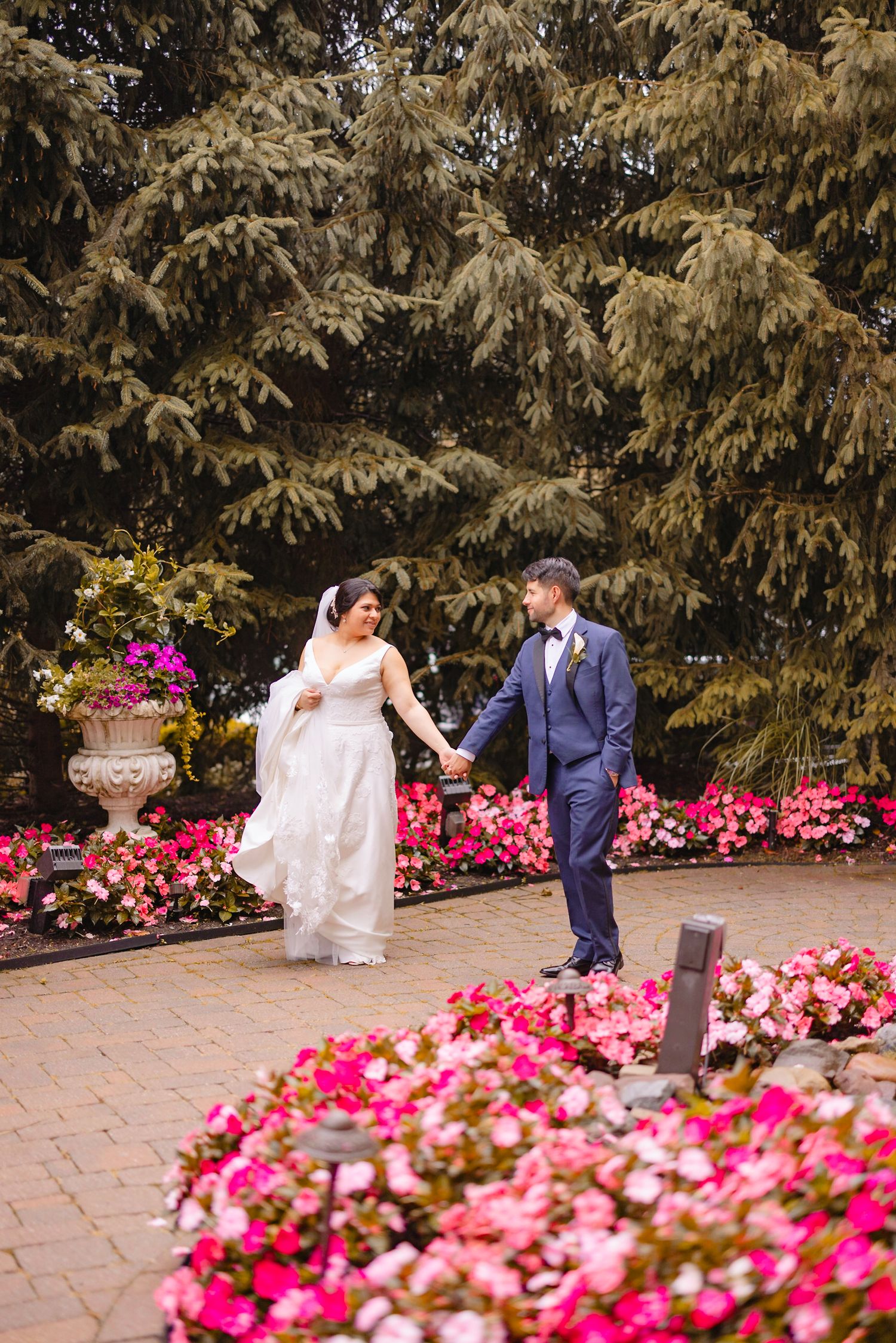 Bride and groom walking hand in hand through a colorful garden with vibrant pink flowers.