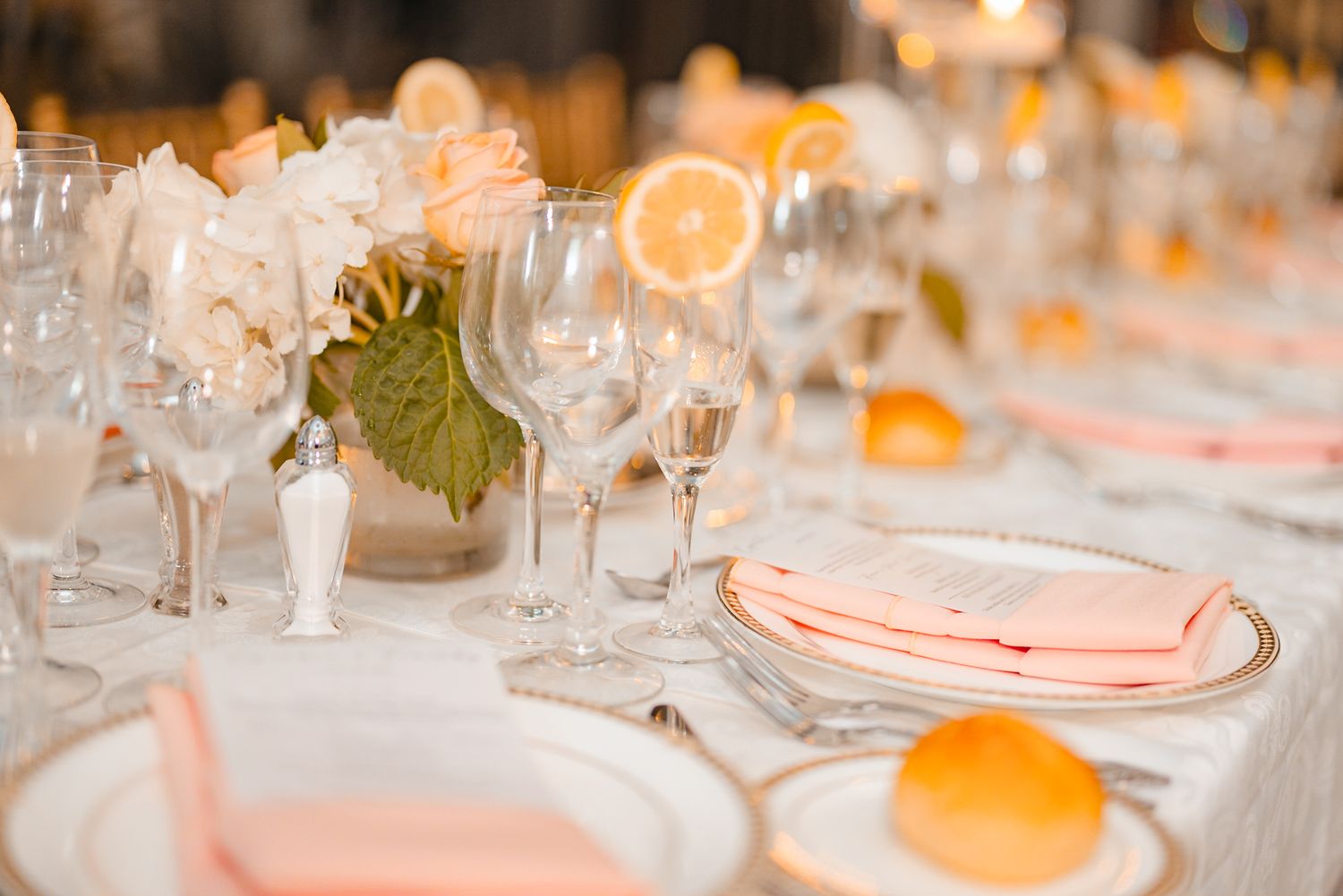 Elegant wedding reception table setting with pink napkins, crystal glasses, and fresh lemons as decor.