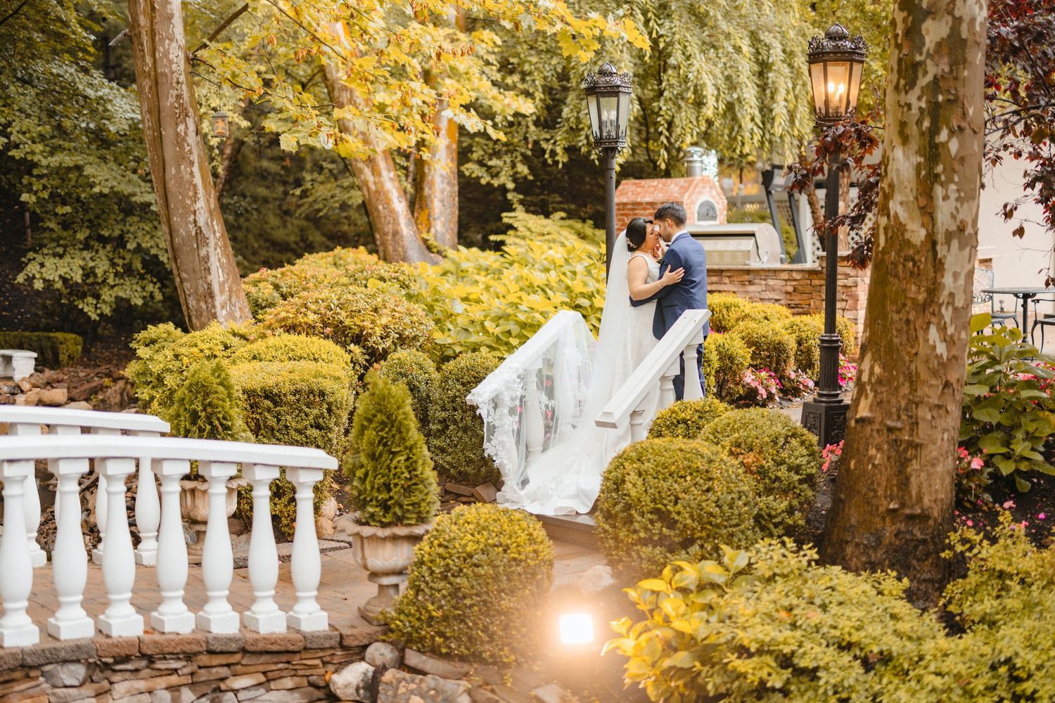 Wedding couple kissing in a beautifully landscaped garden surrounded by manicured shrubs and fall foliage.