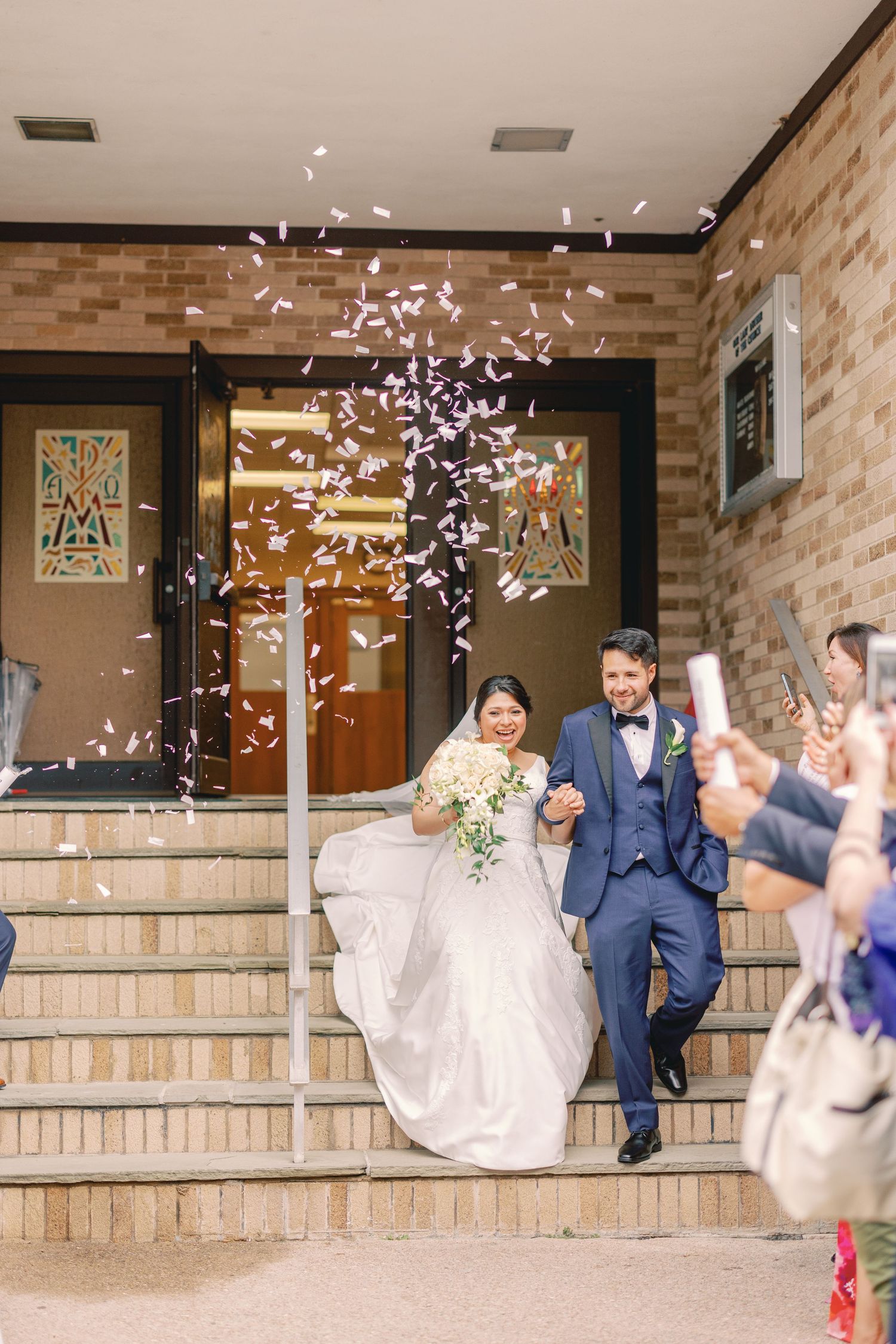 Joyful newlyweds exit church as guests shower them with colorful confetti on the brick steps.
